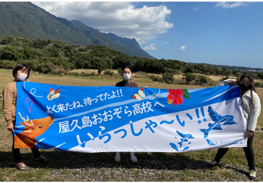 特製の横断幕を掲げて出迎える屋久島おおぞら高等学校の職員